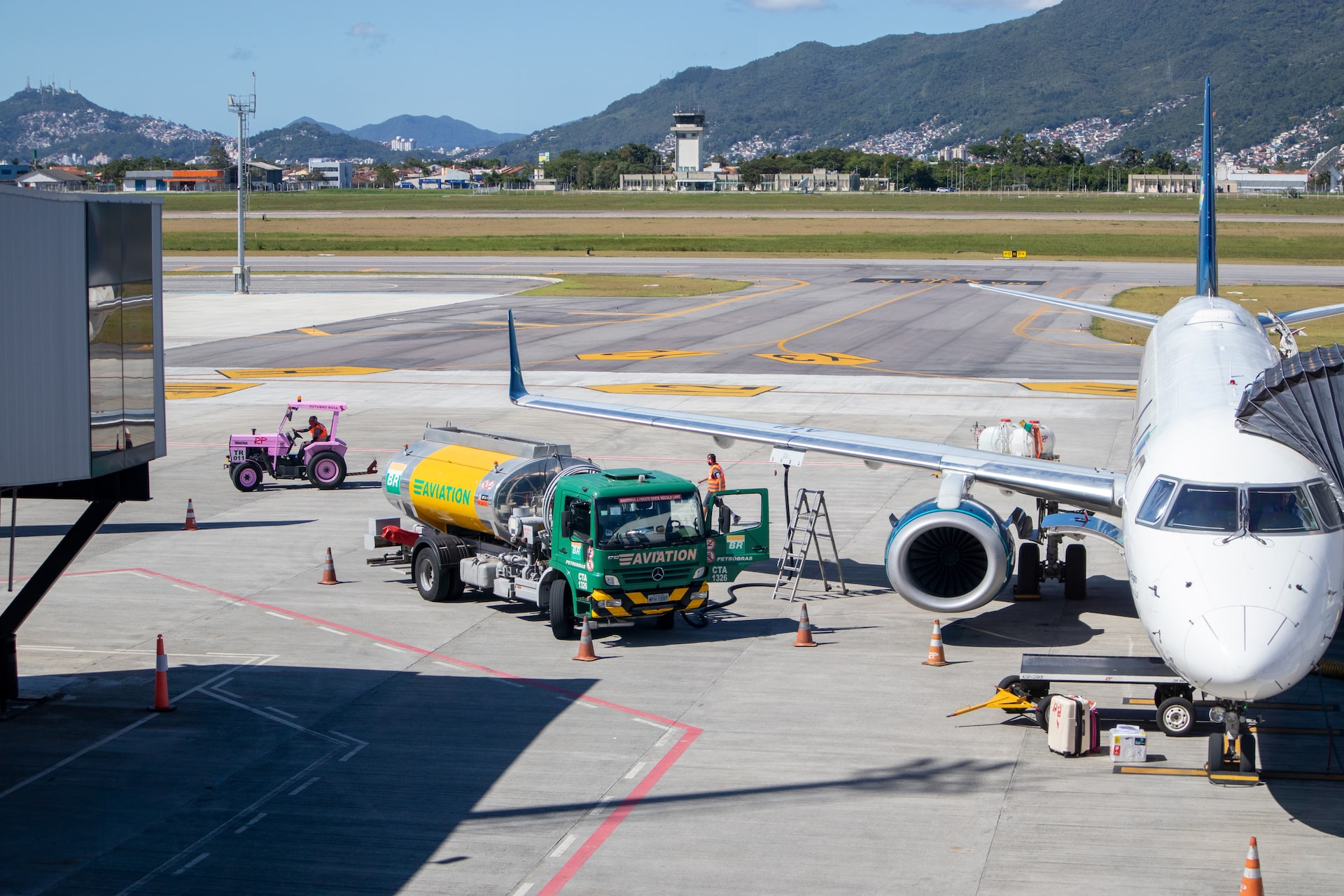 An aircraft being refueled at an airport by a green and yellow fuel truck,