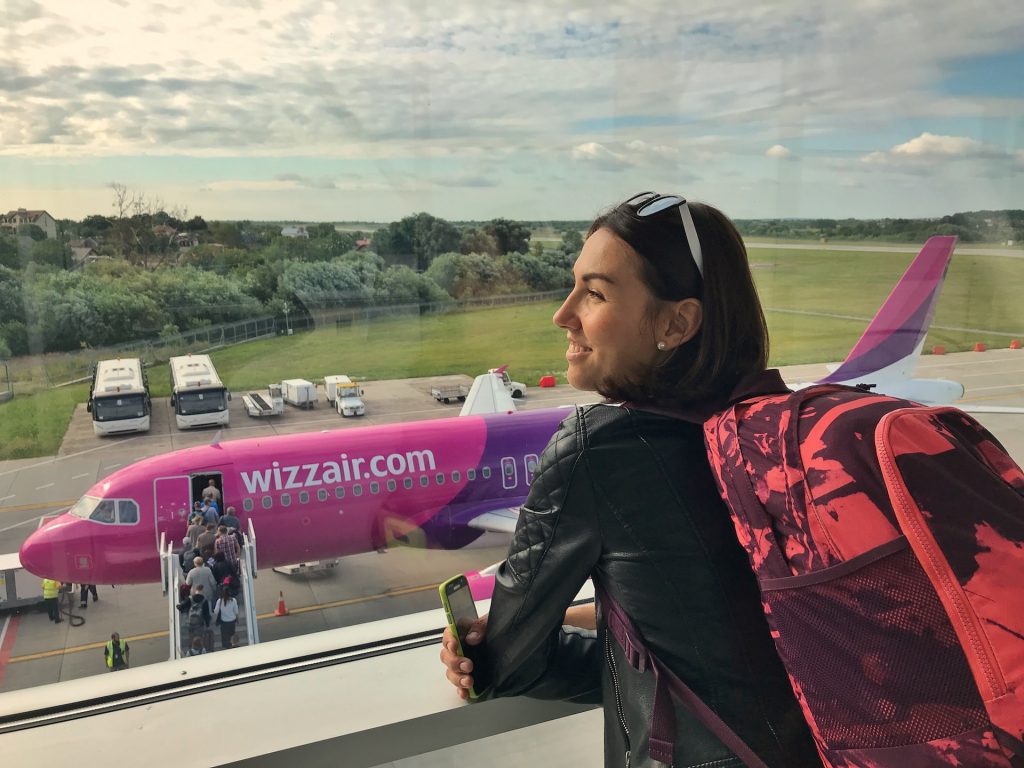 A woman standing in an airport ready to board a Wizzair aircraft with hand luggage.