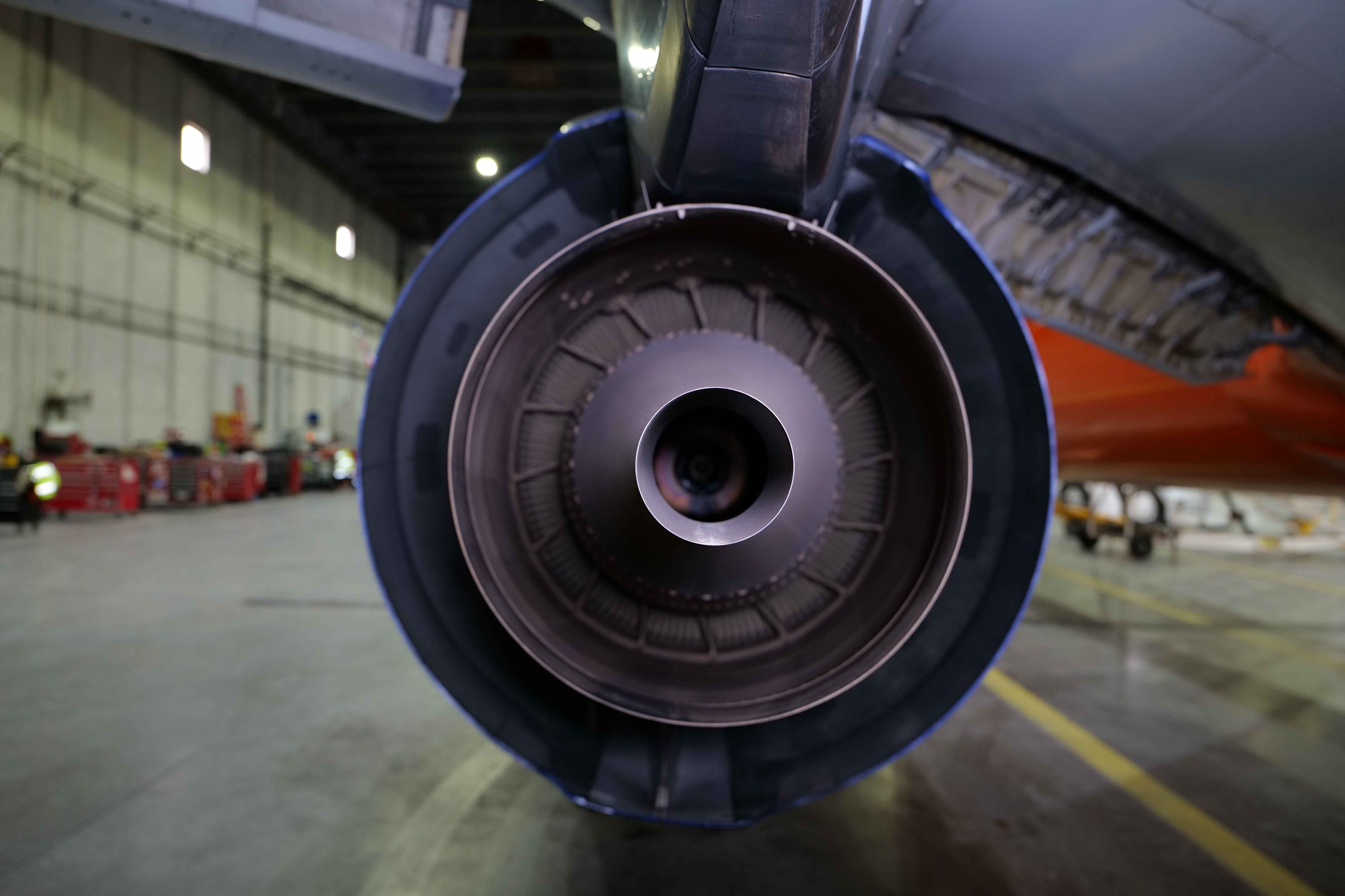 An aircraft engine in the centre, while the aircraft is stationed in a hangar for maintenance.